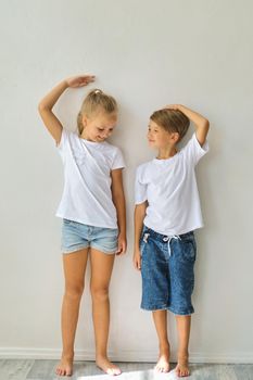 Cool kids, little boy and girl measure their height and compare, have fun near white wall