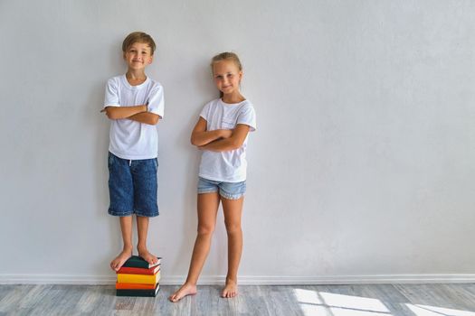 Cool kids, little boy and girl measure their height and compare, have fun near white wall