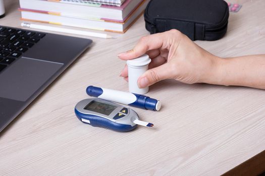 Female hands with a glucometer at the desk. The lifestyle of a person with diabetes, measuring the level of glucose in the blood.