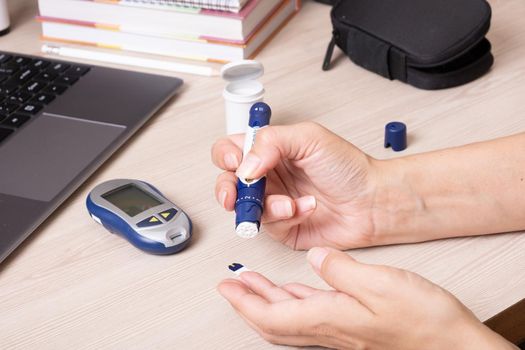 Female hands with a glucometer at the desk. The lifestyle of a person with diabetes, measuring the level of glucose in the blood.