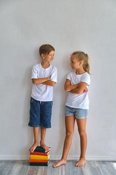Cool kids, little boy and girl measure their height and compare, have fun near white wall