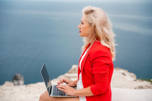 A woman is typing on a laptop keyboard on a terrace with a beautiful sea view. Freelancing, digital nomad, travel and vacation concept