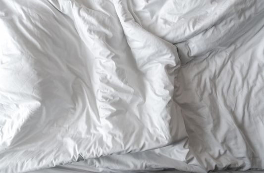 White linen blanket in hotel bedroom. Close-up detail of messy white blanket. Comfortable bed with soft white duvet. Sleep tight with good quality bedding household concept. Wrinkled white blanket.