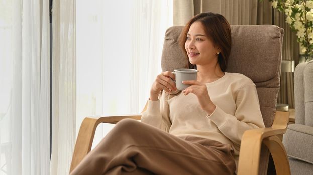 Calm woman in warm sweater drinking hot chocolate, enjoy stress free peaceful mood at home in sunny winter day.