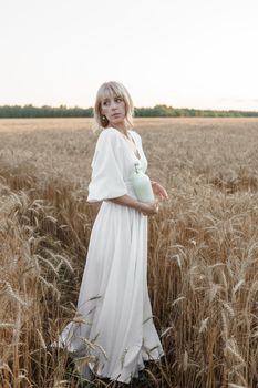 A blonde woman in a long white dress walks in a wheat field. The concept of a wedding and walking in nature.