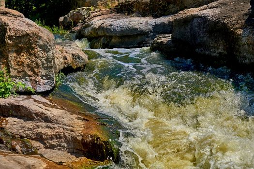 a large natural stream of water flowing in a channel to the sea, a lake, or another such stream. Stormy fast cleaner flow of a mountain river among a stone brown formation.