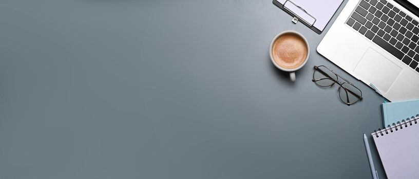 Computer laptop, coffee cup glasses and notebooks on gray background. Copy space.