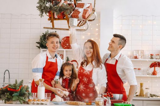 A happy family is standing in the Christmas kitchen and preparing dough for making cookies.