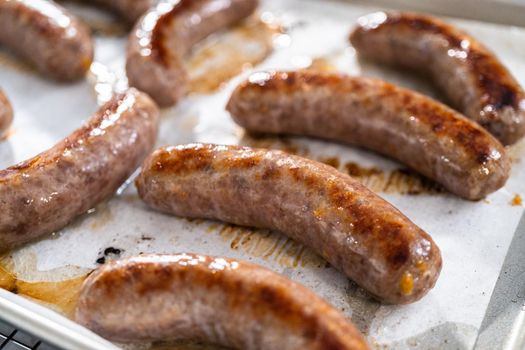 Freshly cooked in oven beer bratwursts on a baking sheet lined with parchment paper.