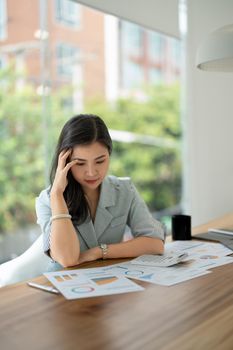 Thoughtful asian woman managing budget and finances using calculator in office, financial accounting concept