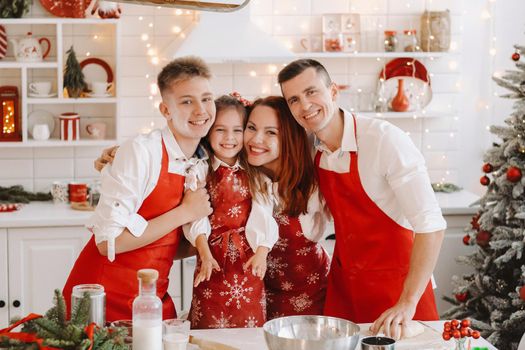 A happy family is standing in the Christmas kitchen and preparing dough for making cookies.