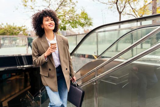 successful business woman smiles leaving the subway station with her briefcase and a coffee in her hand, concept of urban lifestyle and public transport, copy space for text