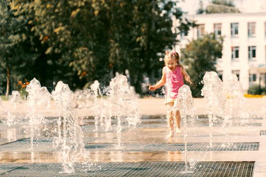 little girl playing with small fountains on the urban plaza. focus on water, baby in blur