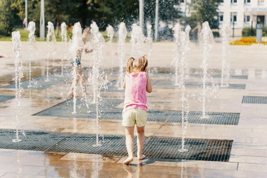 child playing with water in a dry fountain on the urban plaza