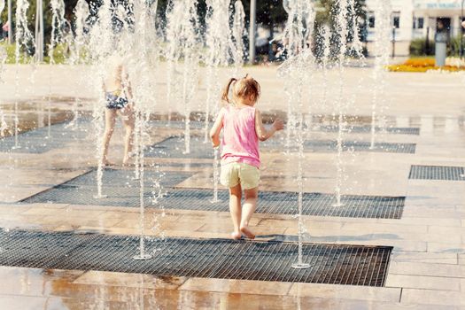 little girl playing with small fountains in the town square on a hot summer day