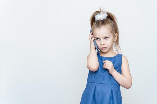 emotional 5-6 year old girl in a blue dress posing in the studio with a smartphone