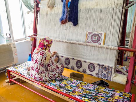 Hands of a woman are weaving carpet tools and threads handmade in Uzbekistan Samarkand Bukhara carpet, textile production folk traditional Muslim work copy space