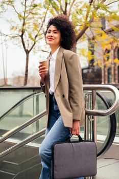 successful business woman smiles entering the subway station with her briefcase and a coffee in her hand, concept of urban lifestyle and public transport