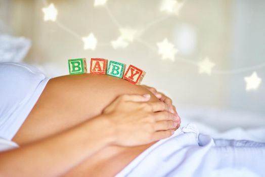 Coming soon. Closeup shot of a pregnant woman lying down with wooden baby blocks on her belly