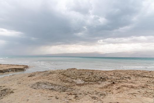 Exotic view of the sinkhole area of the Dead Sea on a stormy winter day. PhotoStorm and rain at the Dead Sea coastline. Salt crystals at sunset. The texture of the Dead sea. Salty seashore. High quality photo