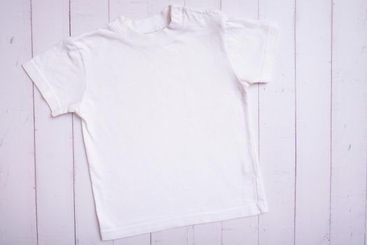 White children's t-shirt mockup for logo, text or design on wooden background top view.