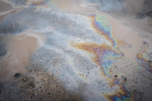 Colored spots of gasoline in a puddle on the background of a broken asphalt road. Environmental pollution concept