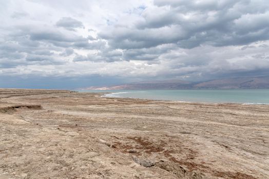 Exotic view of the sinkhole area of the Dead Sea on a stormy winter day. PhotoStorm and rain at the Dead Sea coastline. Salt crystals at sunset. The texture of the Dead sea. Salty seashore. High quality photo