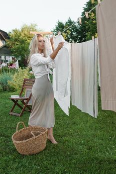 Laundry day. A woman hangs linen and towels on a tree in the courtyard of a village house. Summer cottage concept.