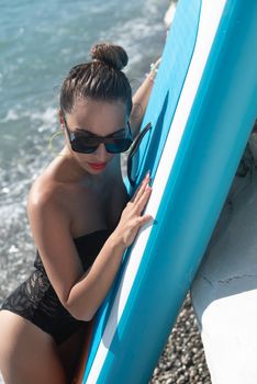 sexy young girl in a swimsuit on a sup board by the sea in stylish sunglasses