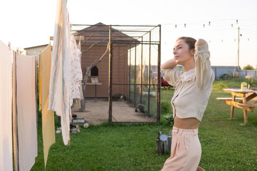 Laundry day. A woman hangs linen and towels on a tree in the courtyard of a village house. Summer cottage concept.