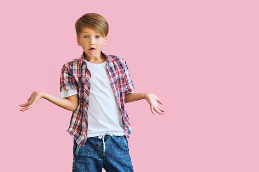 Young happy boy dressed in jeans, a white T-shirt and a plaid shirt with raised hands to the side isolated on pink background with copy space. Blank white t-shirt for your design