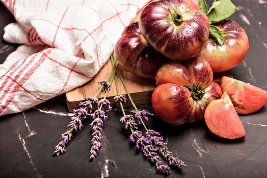 Tiger tomato on a cutting board with basil leaves on wooden background. Fresh tomato wased for cooking. Tomato with droplets of water