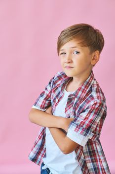 Young happy boy dressed in jeans, a white T-shirt and a plaid shirt isolated on pink background with copy space