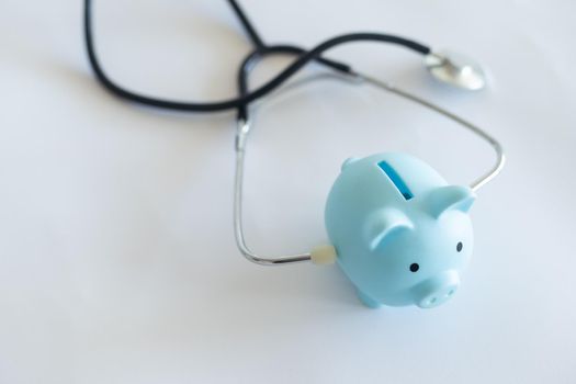 Piggy bank with stethoscope isolated on light blue background with copy space. Health care financial checkup or saving for medical insurance costs concept.