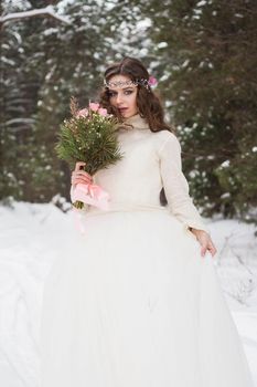 Beautiful bride in a white dress with a bouquet in a snow-covered winter forest. Portrait of the bride in nature.