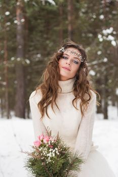 Beautiful bride in a white dress with a bouquet in a snow-covered winter forest. Portrait of the bride in nature.Beautiful bride in a white dress with a bouquet in a snow-covered winter forest. Portrait of the bride in nature.