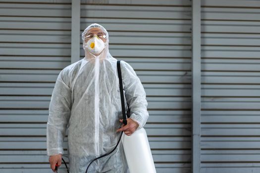 Worker wearing protective suit disinfection gear disinfect surface public place parking. Side view of disinfector safety overall and respiratory mask Covid pandemic disinfection preventive measures