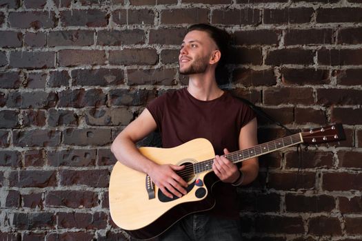 Man with acoustic guitar against brick wall playing music singing songs enjoy life Handsome caucasian male guitar player practice play musical instrument home loft interior Creative lifestyle hobby