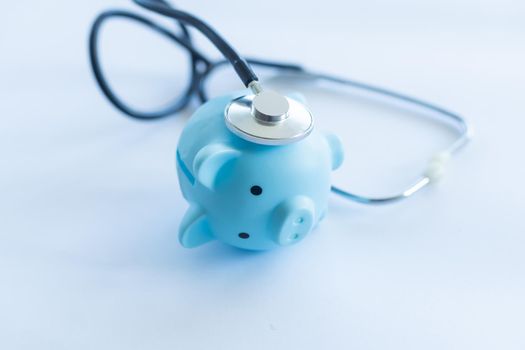 Piggy bank with stethoscope isolated on light blue background with copy space. Health care financial checkup or saving for medical insurance costs concept.