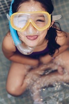 vertical portrait of a beautiful little girl grimacing with snorkel goggles sitting in the tub while taking a bath in the bathtub, kids hygiene concept, copy space for text