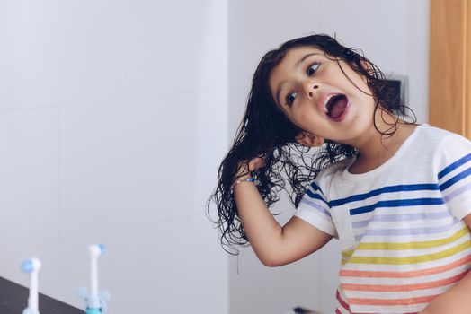 little girl playing with wet hair in front of the mirror after taking a bath, kids hygiene concept, copy space for text