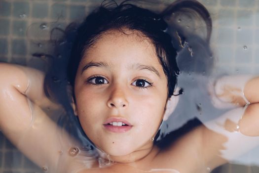 portrait of a happy beautiful little girl lying in the tub while taking a bath in the bathtub, kids hygiene concept