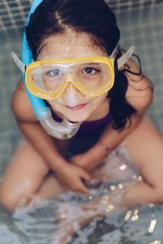vertical portrait of a beautiful little girl smiling with snorkel goggles sitting in the tub while taking a bath in the bathtub, kids hygiene concept, copy space for text