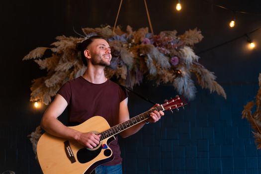 Male musician playing acoustic guitar. Guitarist plays classical guitar on stage in concert Handsome young hipster male guitar player perform private party Stylish long hair Medium shoot