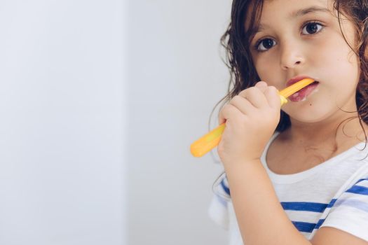 portrait of a little girl brushing her teeth in the bathroom in the morning after shower, kids hygiene concept, copy space for text