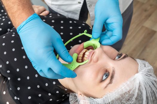 Patient with cheek retractor lying in dentist office in modern clinic