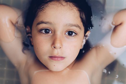 portrait of a happy pretty little girl lying in the tub while taking a bath in the bathtub, kids hygiene concept