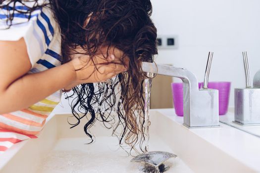 little girl washing her face with water in the bathroom at morning after shower, kids hygiene concept