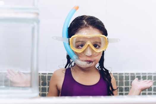 portrait of a funny pretty little girl asking what with snorkel goggles in the tub while taking a bath in the bathtub, kids hygiene concept, copy space for text