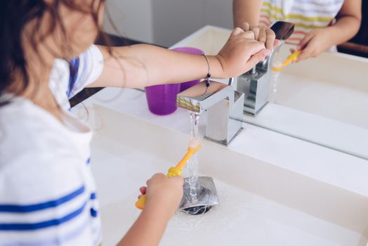 little girl wetting the toothbrush in the bathroom, after taking a shower she prepares to brush her teeth in front of the mirror, kids hygiene concept